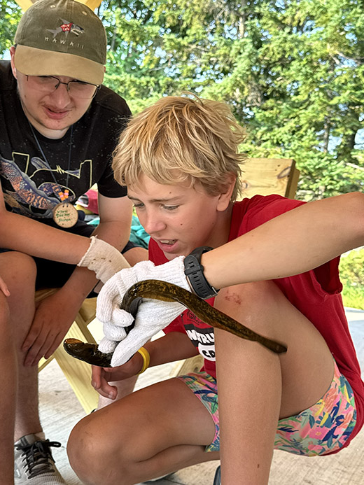 Two teenage boys with inquisitive expressions investigate a live sea lamprey that one boy is holding.